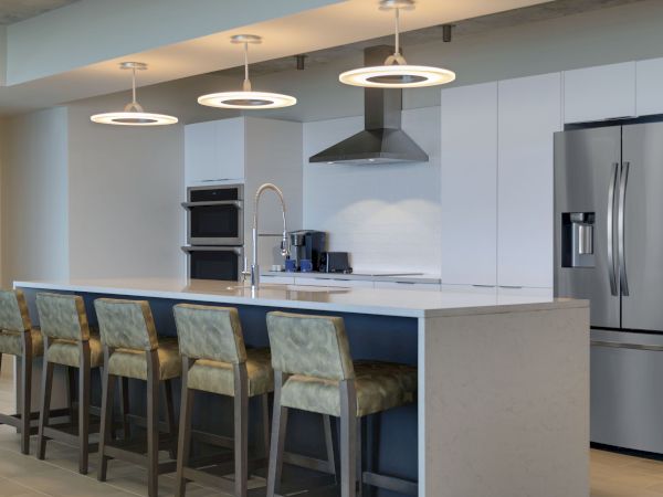 A modern kitchen featuring a large island with four chairs, pendant lighting, stainless steel appliances, and sleek white cabinetry.