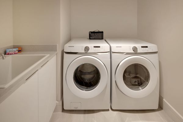 A laundry room with a washer and dryer side by side, a counter with laundry detergent, and a sink, all in a neat and clean setting.