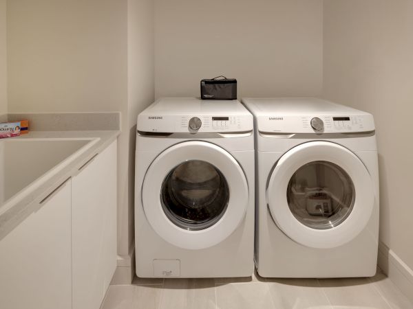 A laundry room with a washer and dryer side by side, a counter with laundry detergent, and a sink, all in a neat and clean setting.