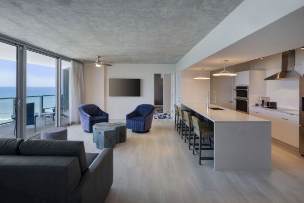 A modern open-concept living area with ocean views, featuring a kitchen, seating area, TV, and balcony access.