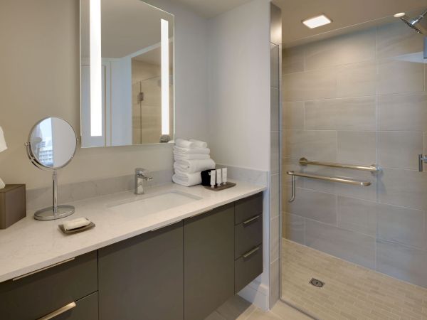 A modern bathroom with a walk-in shower, vanity with a countertop, toiletries, a mirror with lighting, and a magnifying mirror on the counter.