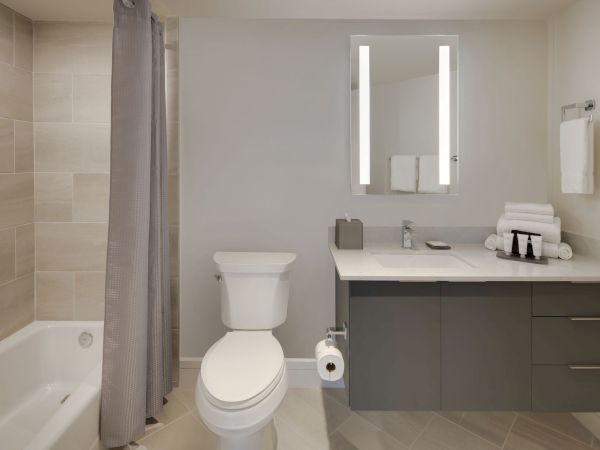 A modern bathroom with a bathtub, toilet, sink, large mirror, and countertop items like towels and toiletries.