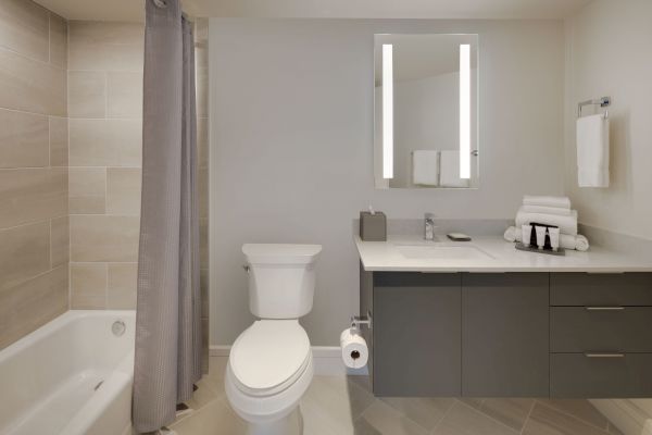 A modern bathroom with a bathtub, shower curtain, toilet, vanity with a sink, mirror, and folded towels.