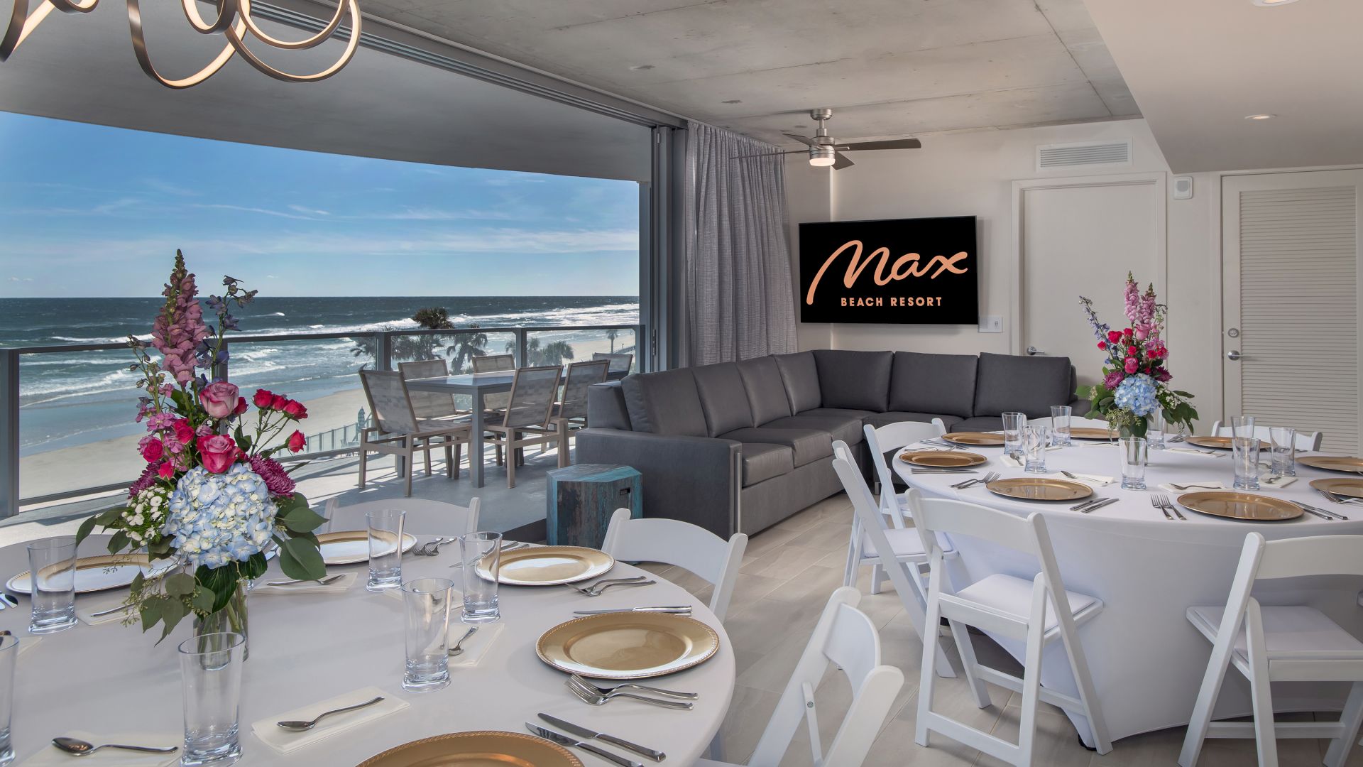 A modern dining area with elegantly set tables, floral centerpieces, and a spacious balcony with ocean views. A "Max Grand Resort" sign is visible.