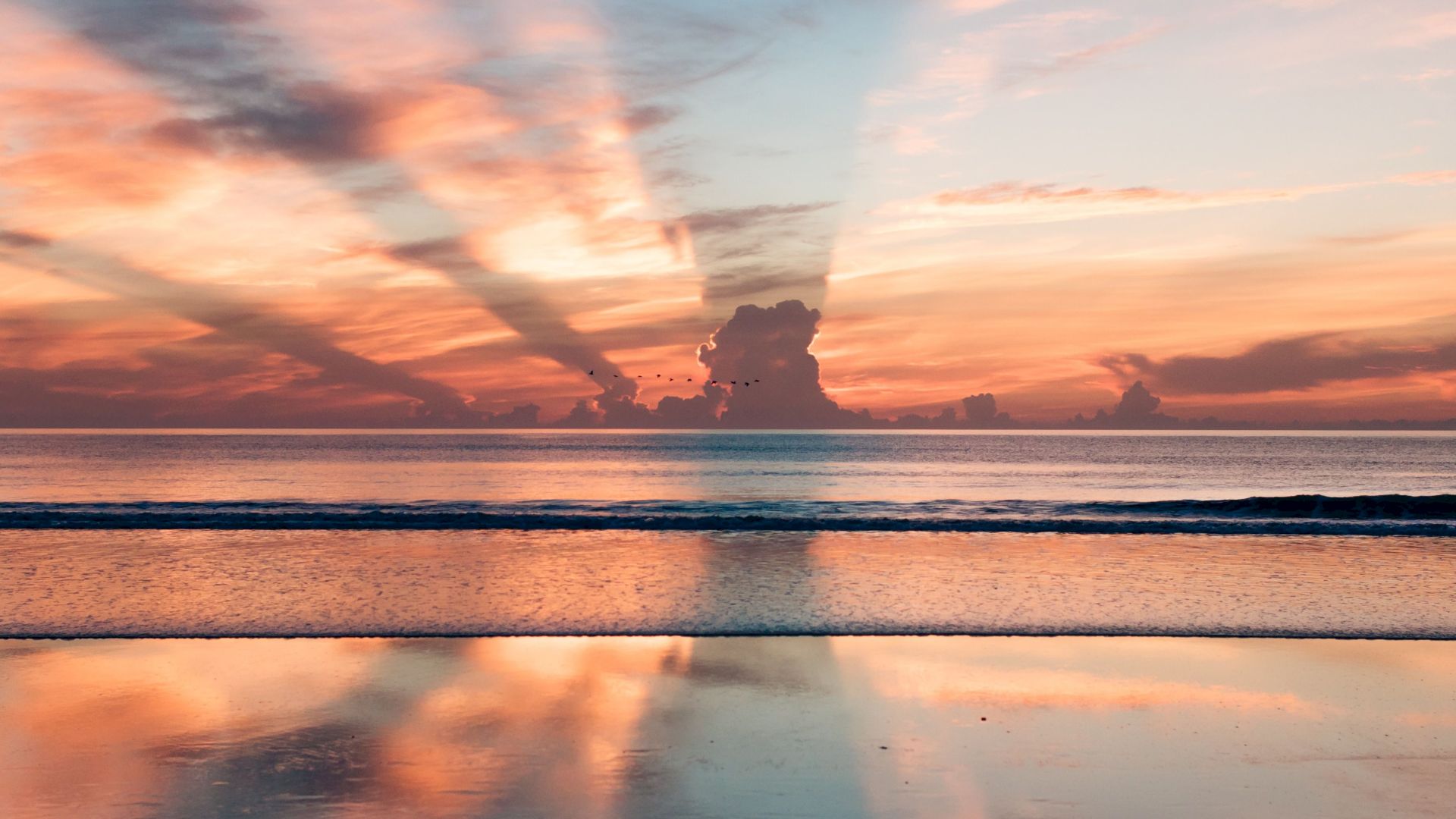 A serene beach sunset with colorful hues and clouds reflecting in the water, creating a peaceful and picturesque scene.