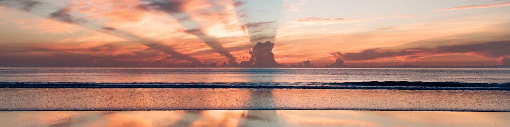 A serene beach sunset with colorful hues and clouds reflecting in the water, creating a peaceful and picturesque scene.