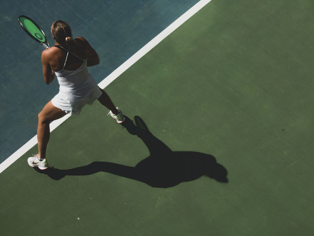 A person in athletic wear is playing tennis on a court, holding a racket and preparing to hit a shot.