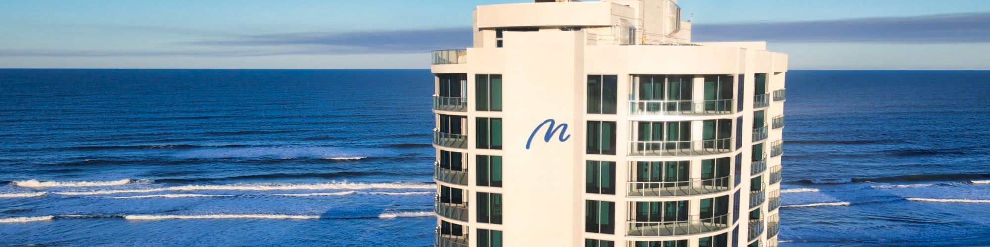 The image shows a tall beachfront building with balconies and a blue 