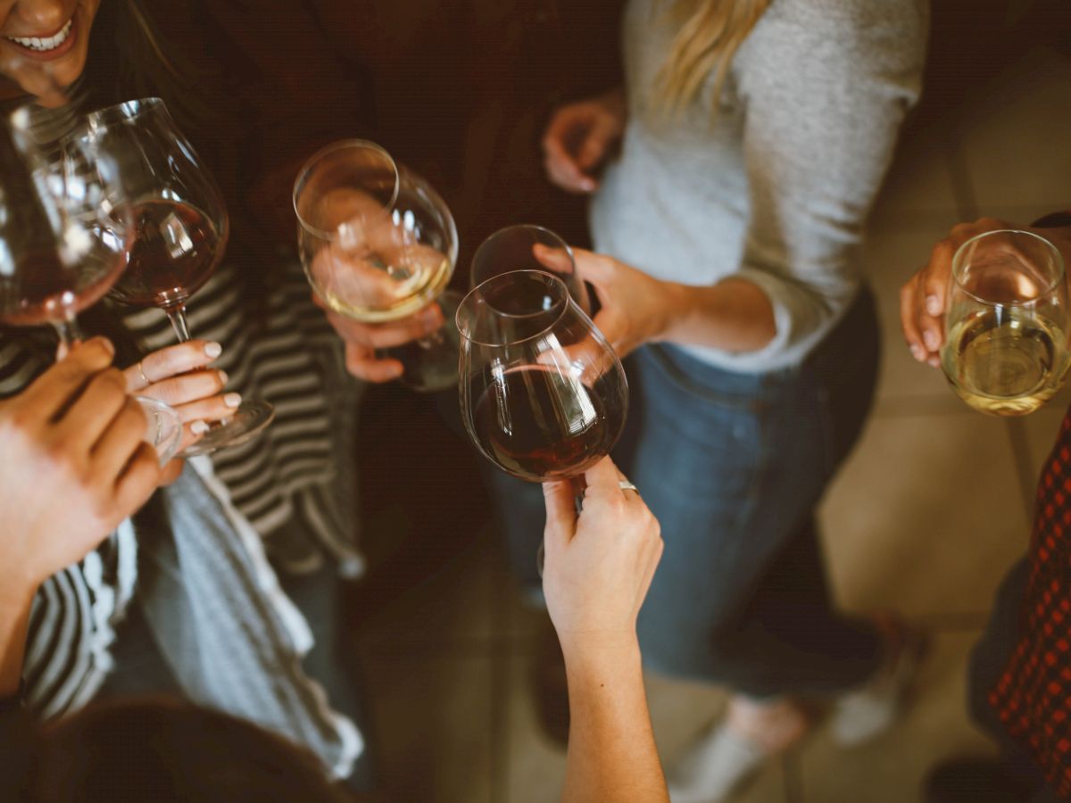 A group of people holding wine glasses, gathered in a casual setting, engaging in a toast or conversation.