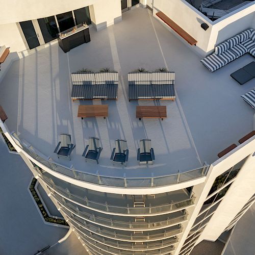 Aerial view of a spacious rooftop patio with seating, lounge chairs, and striped cushions on a curved building.