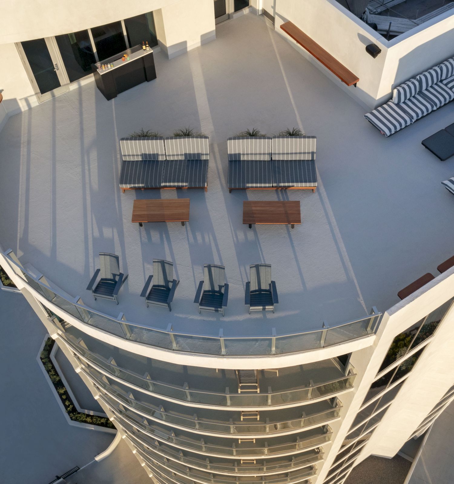 This image shows a rooftop terrace with seating areas, tables, lounge chairs, and a small outdoor kitchen.