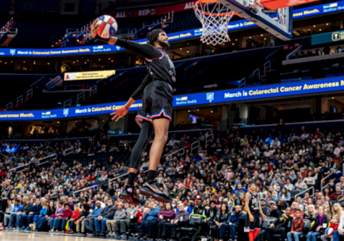 A basketball player shoots in an arena while the crowd watches and banners read &ldquo;March is Colorectal Cancer Awareness Month.&rdquo;