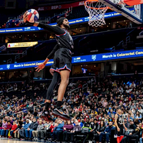 A basketball player shoots in an arena while the crowd watches and banners read &ldquo;March is Colorectal Cancer Awareness Month.&rdquo;