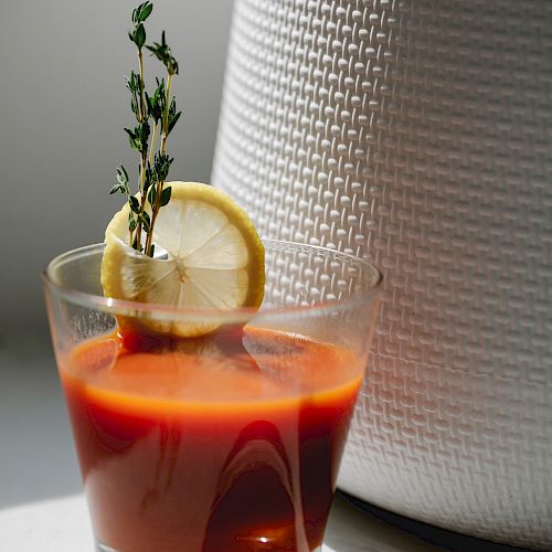 A glass of tomato juice garnished with a lemon slice and sprig of thyme, placed in a well-lit setting.