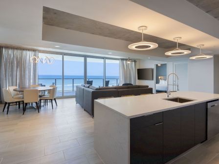 Modern open-plan kitchen and living area with a view of the ocean, featuring contemporary furnishings, a dining table, and large windows.