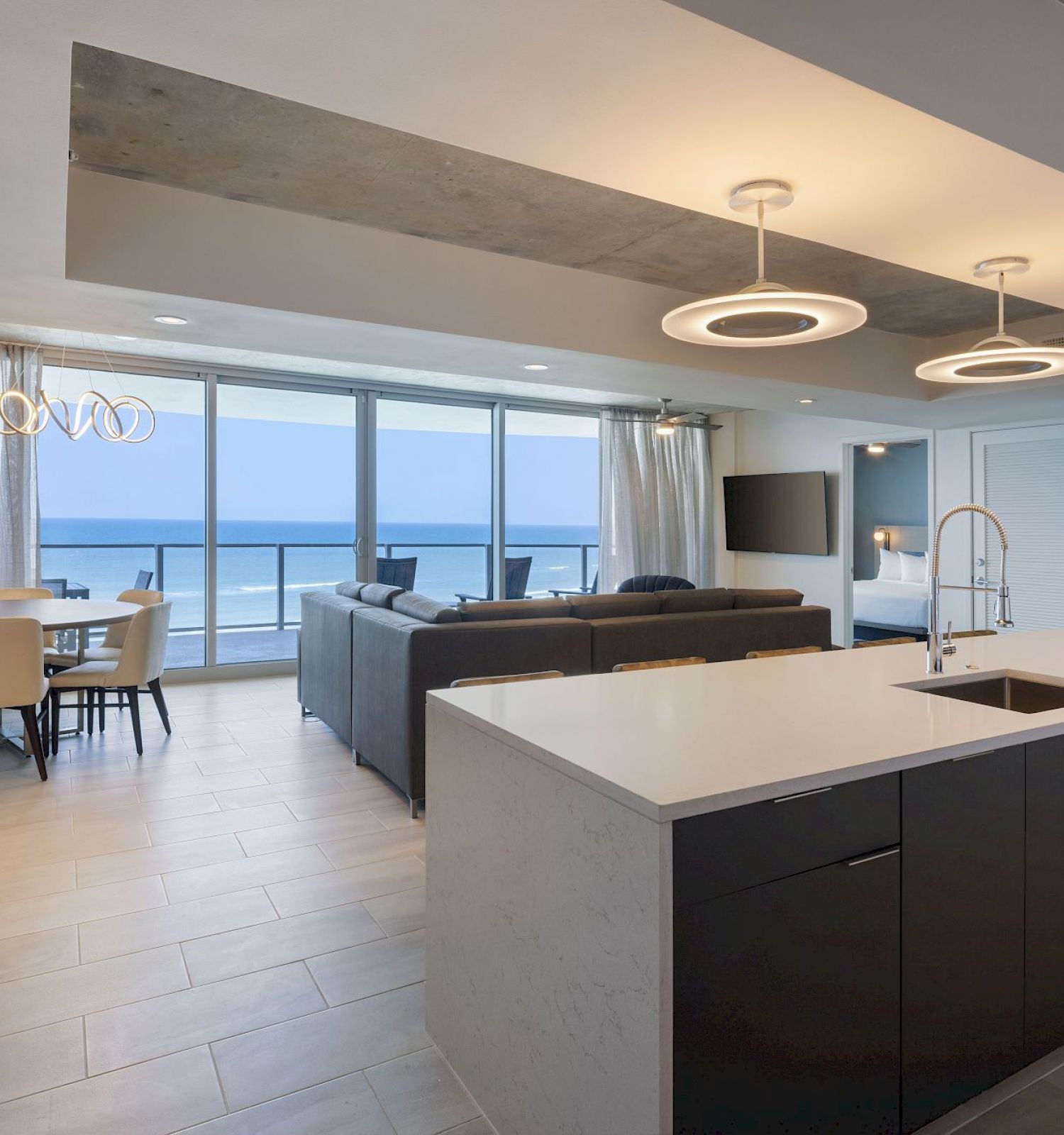 Modern open-plan living area with a kitchen island, dining table, living room, and large windows overlooking an ocean view.