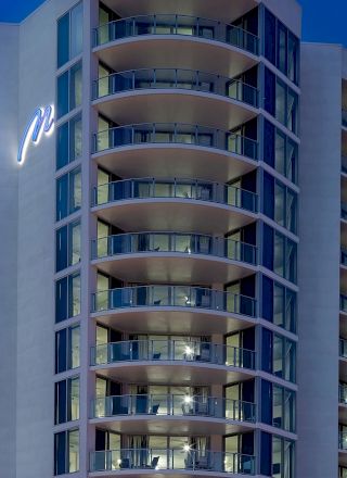 A modern high-rise building with illuminated balconies and a stylized letter "P" on the exterior, set against a twilight sky.