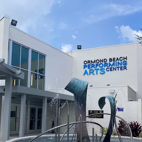 A white civic building labeled Ormond Beach Performing Arts Center, with a decorative fountain and blue sky behind it.