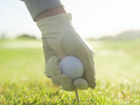 A person wearing a golf glove is placing a golf ball on a tee on a grassy golf course.