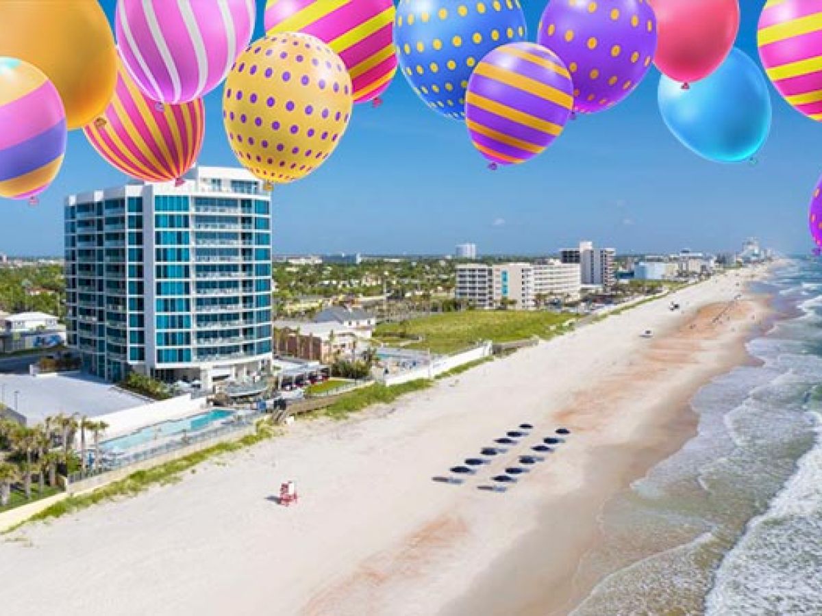 A beachside cityscape with a modern building, decorated with colorful balloons in the sky above.