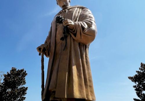A statue of a person holding a cane, surrounded by trees under a clear blue sky.