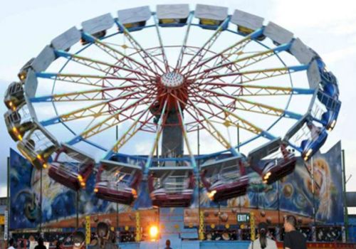 An amusement park ride with spinning gondolas, featuring colorful lights and cosmic-themed artwork, observed by visitors.