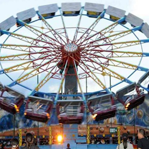 An amusement park ride with spinning gondolas, featuring colorful lights and cosmic-themed artwork, observed by visitors.