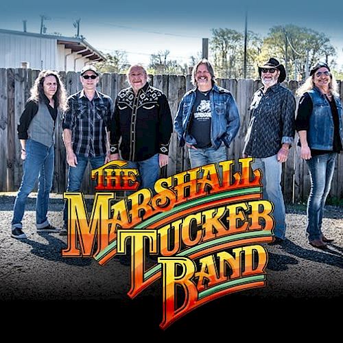 Six people are posing in a line outdoors with "THE MARSHALL TUCKER BAND" logo displayed in front of them.