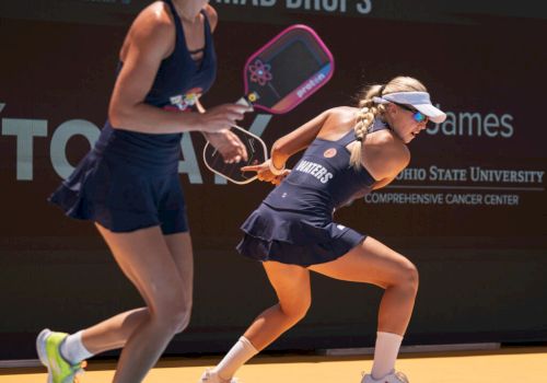 Two women are playing pickleball on an outdoor court, both wearing sports attire and holding paddles.