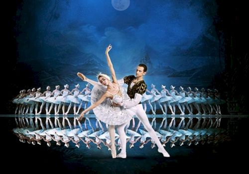 A ballet performance with a pair in the foreground and multiple dancers in a line behind, set against a moonlit blue background.