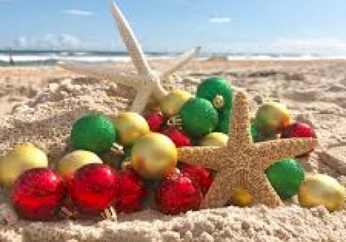 A sandy beach with colorful Christmas ornaments and starfish, representing a festive holiday scene under a clear blue sky.