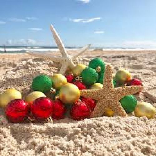 A sandy beach with colorful Christmas ornaments and starfish, representing a festive holiday scene under a clear blue sky.