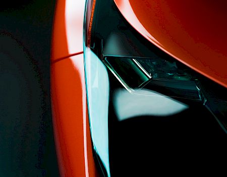 The image shows a close-up view of a sleek, red car's headlight with glossy detailing and sharp features.