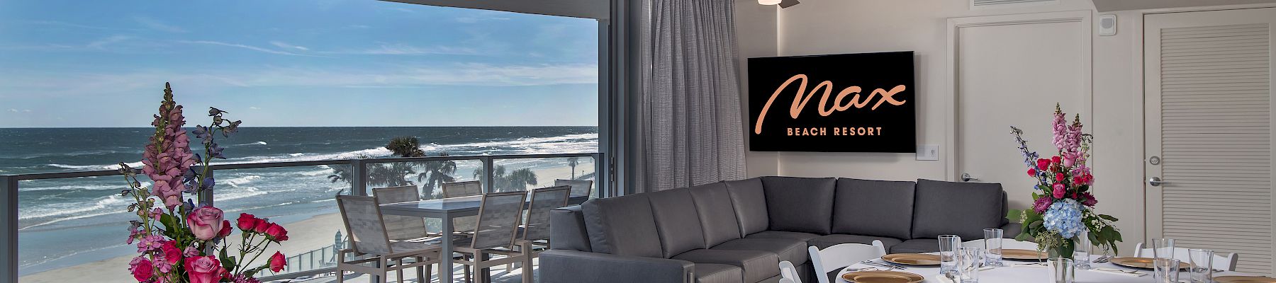 A modern dining area with ocean views, elegant table settings, floral centerpieces, and a sign that reads 