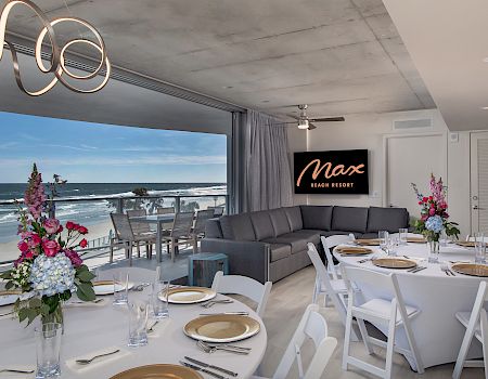 A modern dining area with ocean views, elegant table settings, floral centerpieces, and a sign that reads 