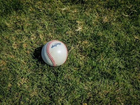 A baseball sits on a grassy field, with its red stitching clearly visible.