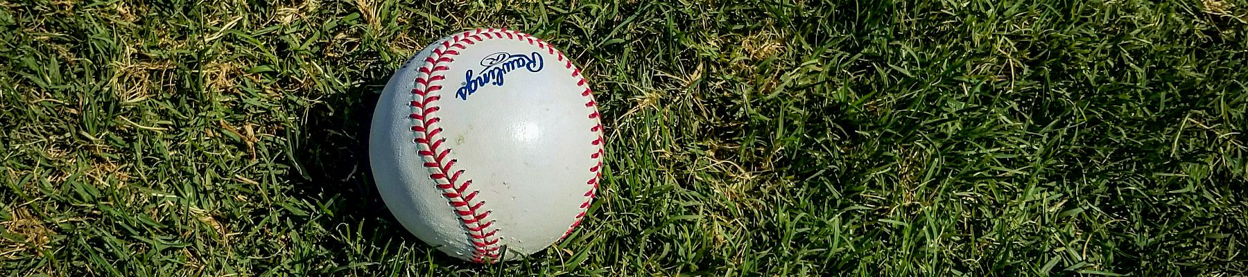 A baseball with visible stitching is resting on a patch of grass.