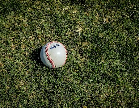 A baseball with visible stitching is resting on a patch of grass.