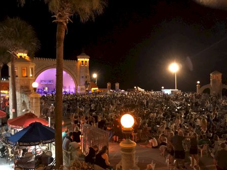 A large crowd gathers at an outdoor venue with a castle-like structure, lit by street lamps; people appear to be enjoying a nighttime event.