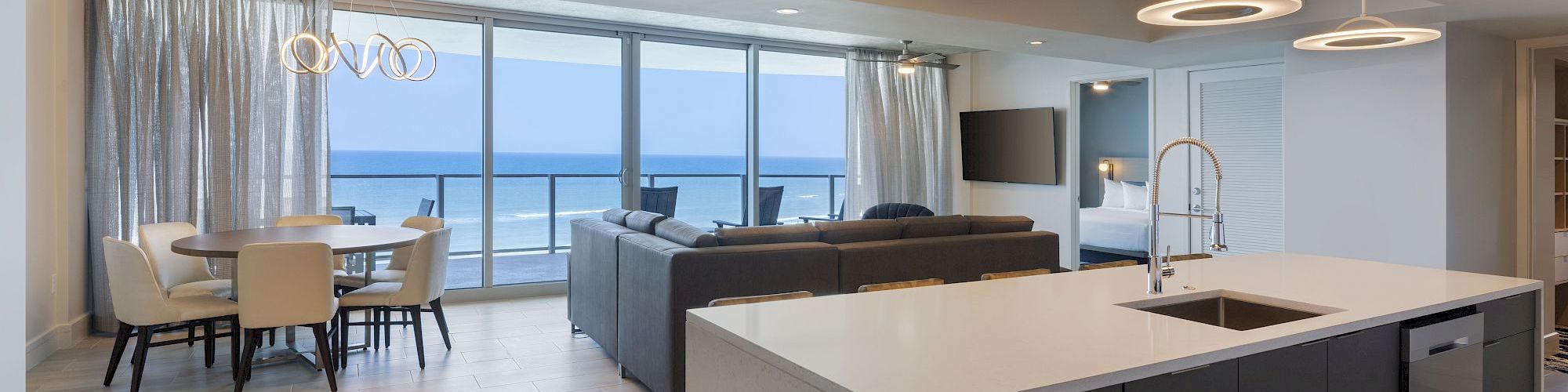 Modern open-concept living and dining area with ocean view, featuring a kitchen island, dining table, and large windows.