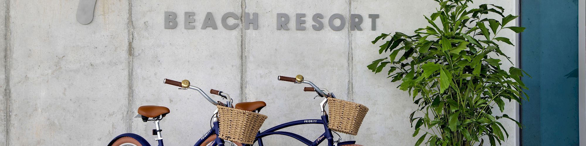 The image shows two bicycles with baskets parked near a wall with the text 