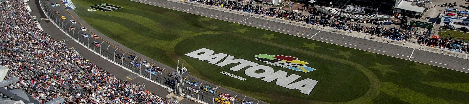 This image shows a race track with cars lined up, a large crowd in the stands, and 