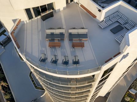 A top-down view of a modern rooftop patio with seating areas, tables, and sun loungers. The space is designed for relaxation and socializing.