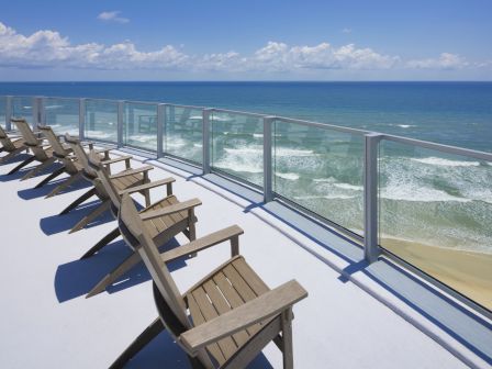 A rooftop deck overlooking the ocean with wooden lounge chairs arranged in a row, all facing out towards the expansive and scenic ocean view.