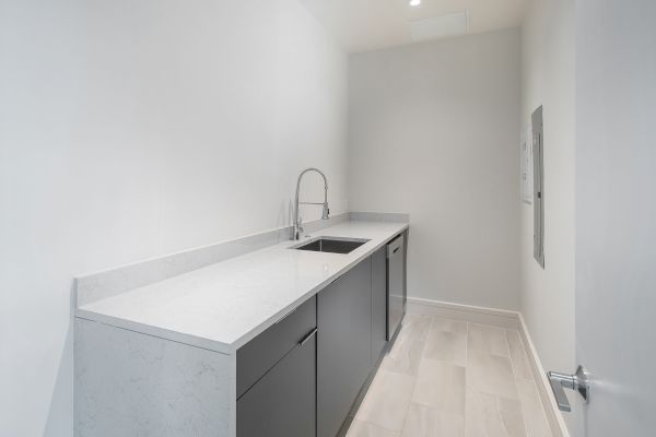 A modern, narrow kitchen with a sleek countertop, integrated sink, minimalist cabinetry, and light flooring.