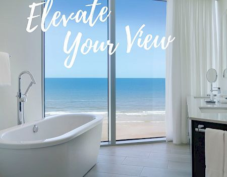 A bathroom with a freestanding tub and a large window overlooking the ocean. Text reads 