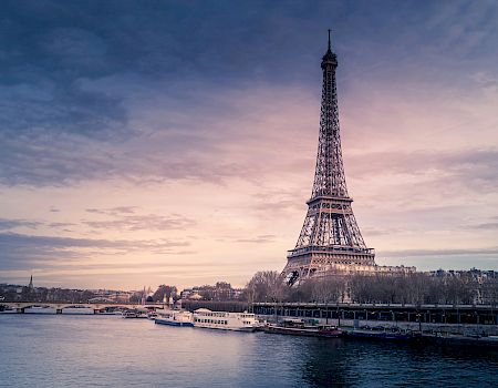 The image contains the Eiffel Tower in Paris, France, with the Seine River in the foreground and a beautiful sunset in the background.