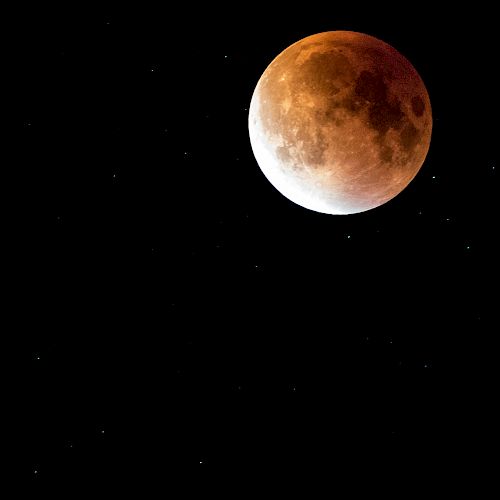 The image shows a lunar eclipse, with the moon appearing reddish-orange against a black sky dotted with stars.