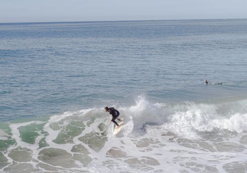 A person is surfing on a wave in the ocean, with another surfer visible in the background to the right.