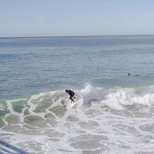 A person is surfing on a wave in the ocean, with another surfer visible in the background to the right.